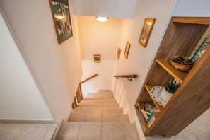 A staircase with a wooden handrail, a light fixture above, and a shelf with decorative items.