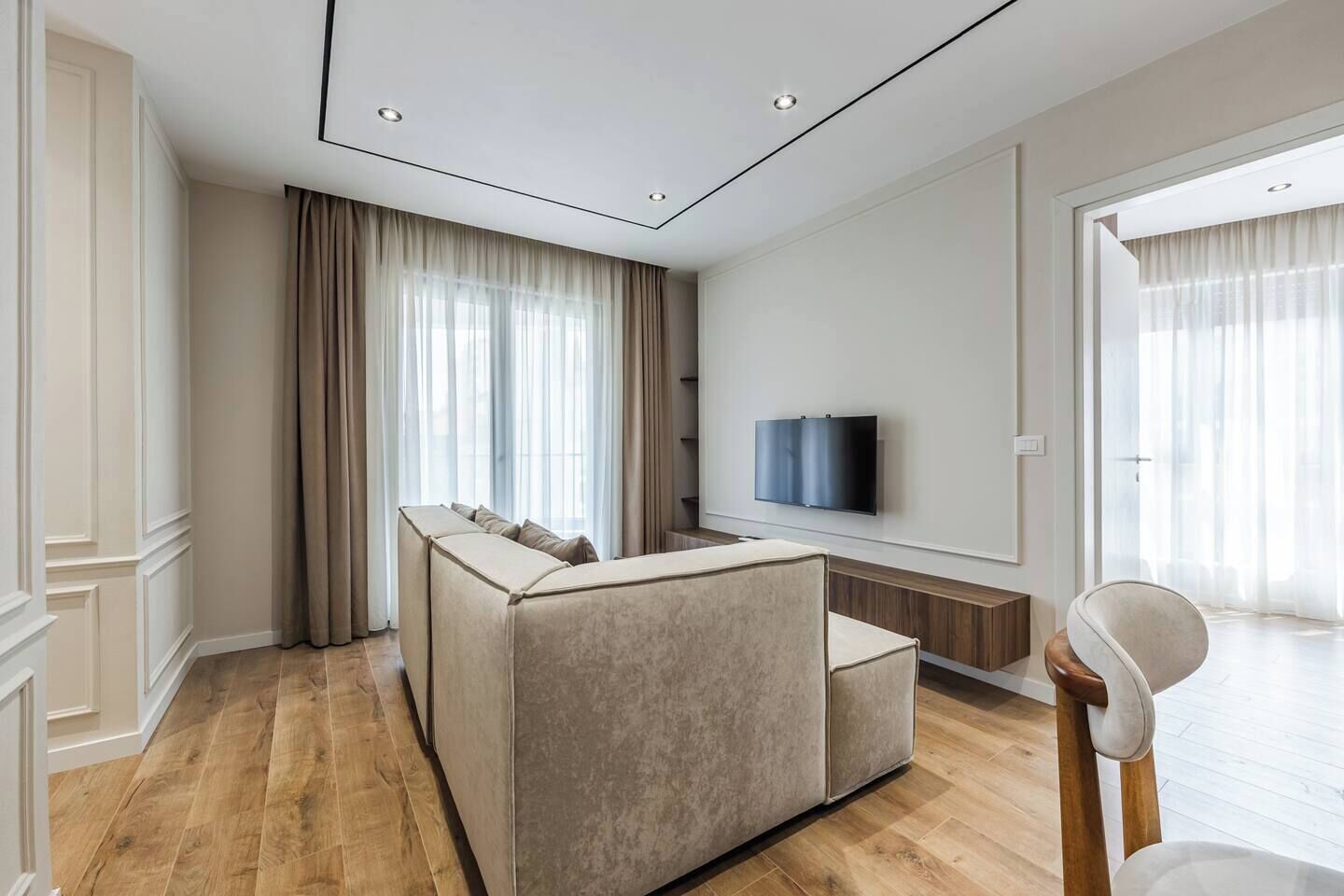 Una sala de estar moderna con un sofá, un televisor fijado a la pared y piso de madera.