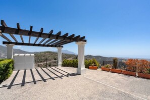 Ein überdachter Außenbereich mit einer Pergola, weißen Säulen und Blumentöpfen.