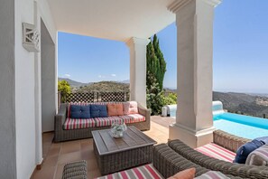 Ein überdachter Außenbereich mit Pool, Korbmöbeln und Blick auf die Landschaft.