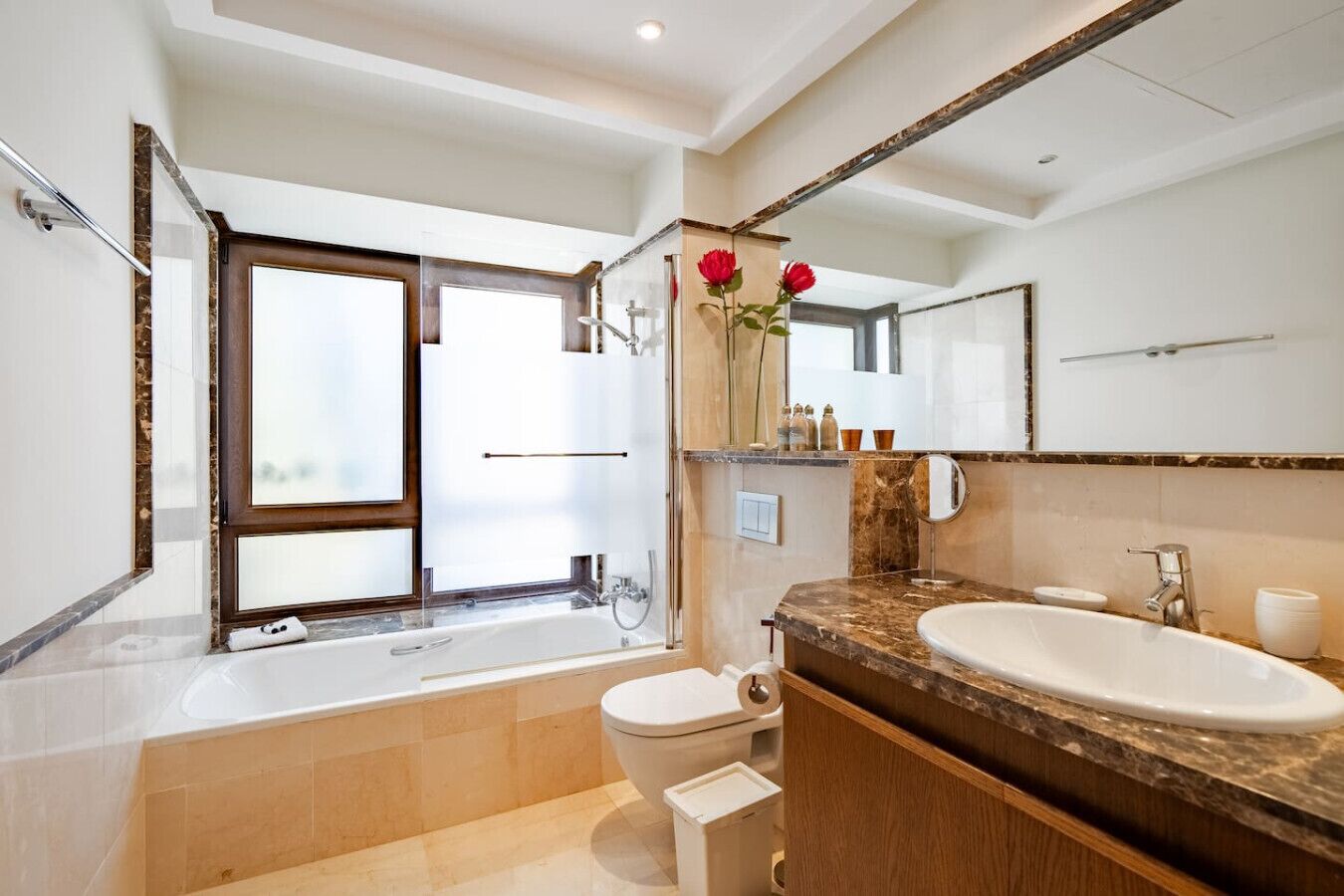 A modern bathroom with a bathtub, a sink, a toilet, and a large mirror.