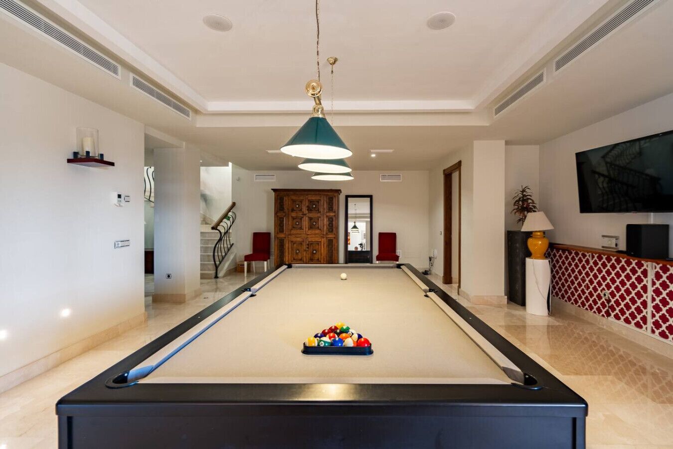 Una mesa de billar con bolas, un televisor y una escalera que sube a un nivel superior.