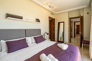Ein Hotelzimmer mit einem großen Bett, einem Nachttisch, einer Lampe, einem Spiegel und einer Tür zu einem anderen Raum.