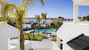 A pool area with a clear sky, palm trees, and white buildings with balconies. - ESTEPONA SUNSETS - BRAND-NEW MODERN 3-BEDROOM APARTMENT (Estepona)