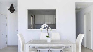 A dining area with a white table, four chairs, and a potted orchid. - ESTEPONA SUNSETS - BRAND-NEW MODERN 3-BEDROOM APARTMENT (Estepona)