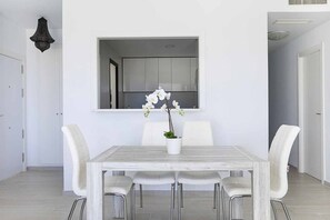 A dining area with a white table, four chairs, and a potted orchid. - ESTEPONA SUNSETS - BRAND-NEW MODERN 3-BEDROOM APARTMENT (Estepona)