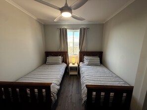 A small, well-lit room with two single beds, a ceiling fan, and a window with curtains.