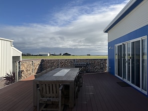 A deck with a table and chairs, a stone wall, and a view of a grassy field under a cloudy sky.