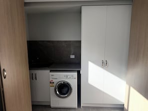 A compact laundry room with a washing machine, cabinets, and a tiled backsplash.