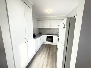 A compact kitchen with white cabinets, a built-in oven, and a refrigerator.