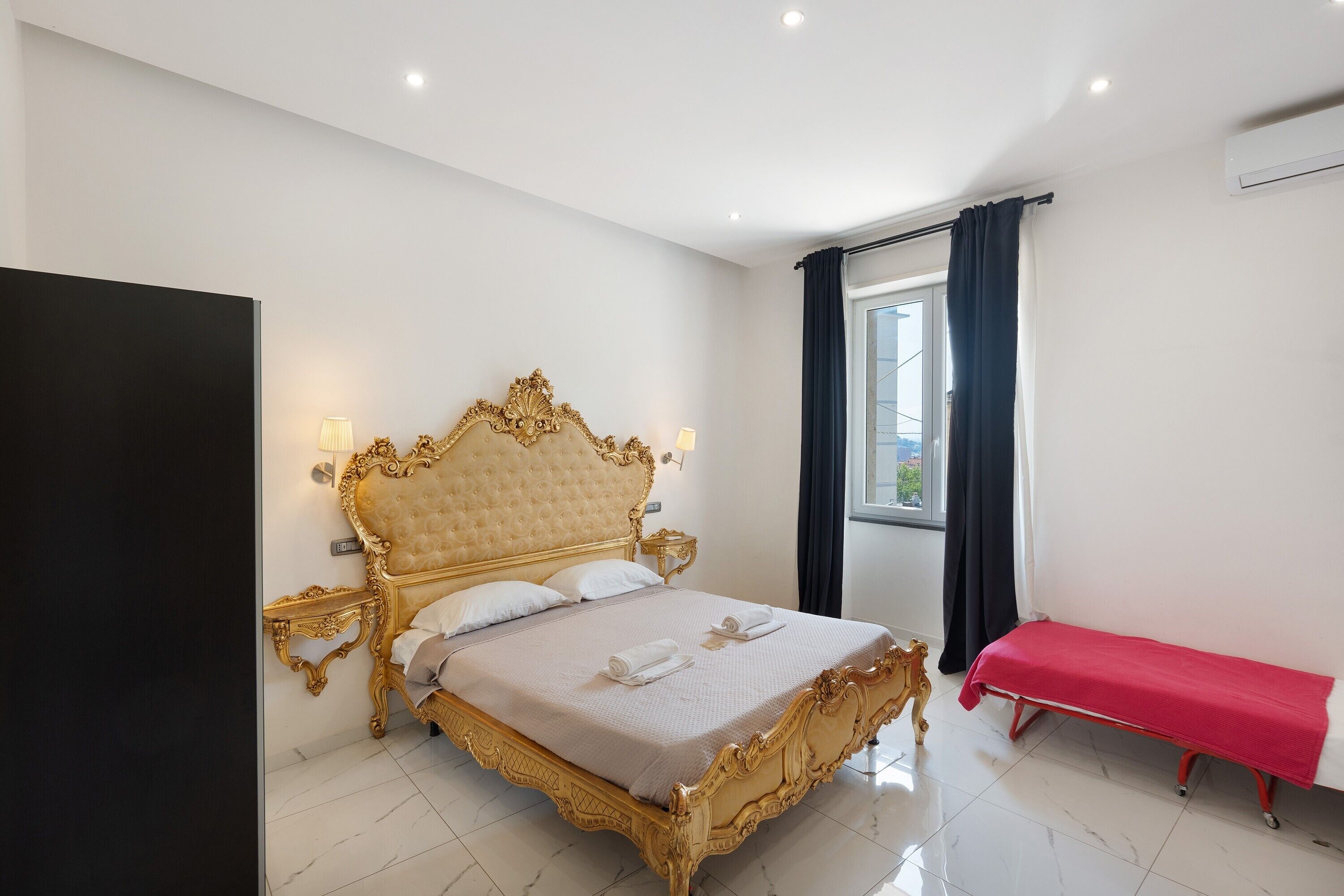 Um quarto espaçoso com uma cama grande, mesas de cabeceira, um banco e uma janela com cortinas.