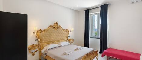Une chambre spacieuse avec un grand lit, des tables de chevet, un banc et une fenêtre avec des rideaux.