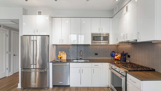 A modern kitchen with stainless steel appliances, white cabinetry, and a wooden countertop.