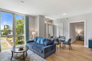 A modern living room with a sofa, chairs, a dining table, and large windows.