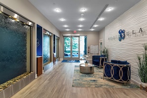 A modern reception area with a glass door entrance, a reception desk, and a seating area with blue upholstered chairs.