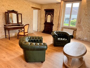 Ein Zimmer mit Steinwand, einem Holztisch, zwei Ledersesseln und einem Spiegel.
