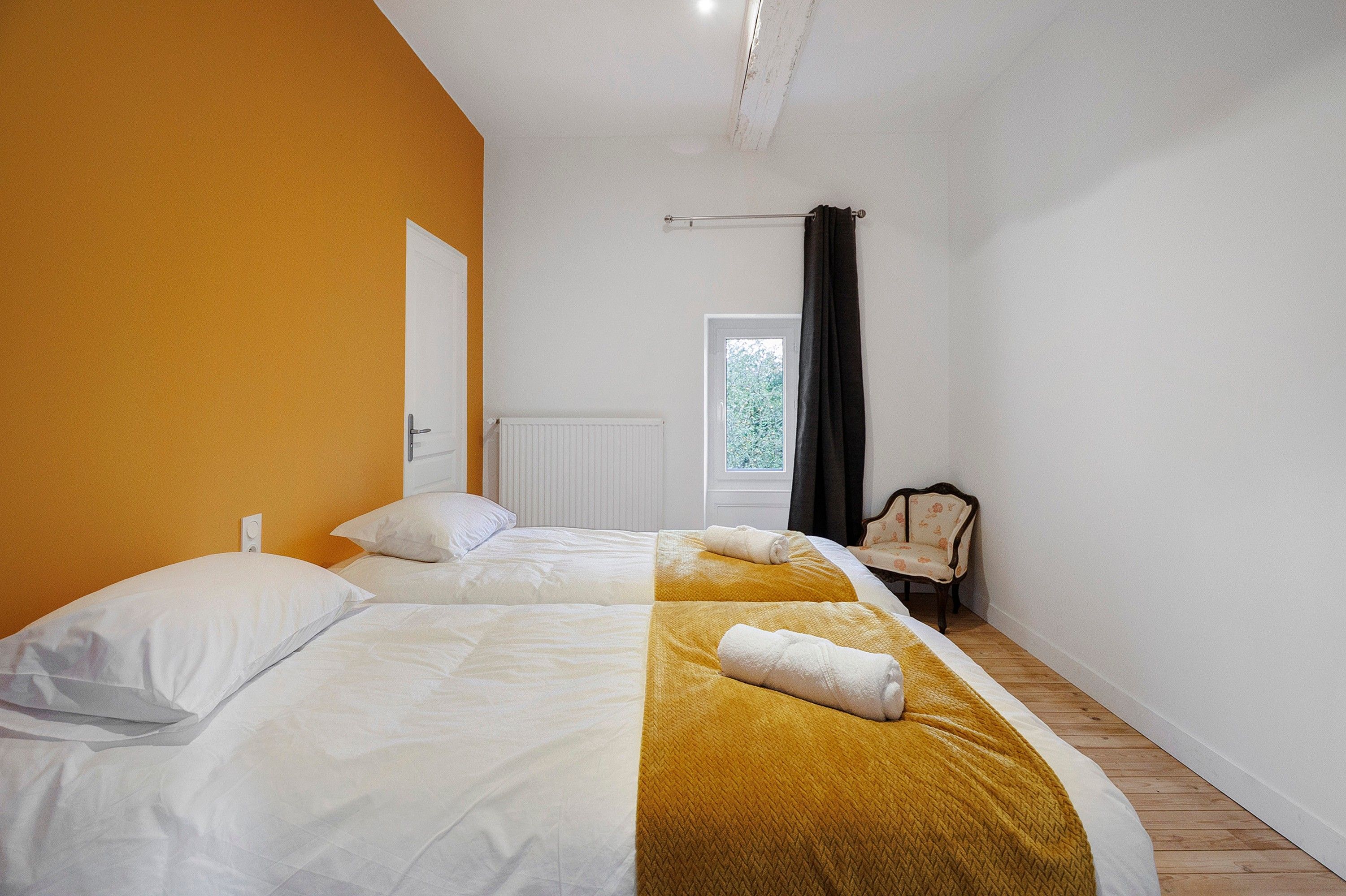 Een slaapkamer met twee bedden, een radiator, een raam met gordijnen en een stoel.
