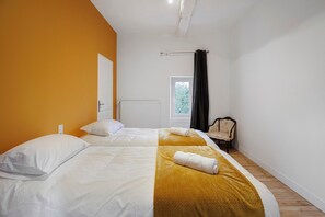 Ein Schlafzimmer mit zwei Betten, einem Heizkörper, einem Fenster mit Vorhängen und einem Sessel.