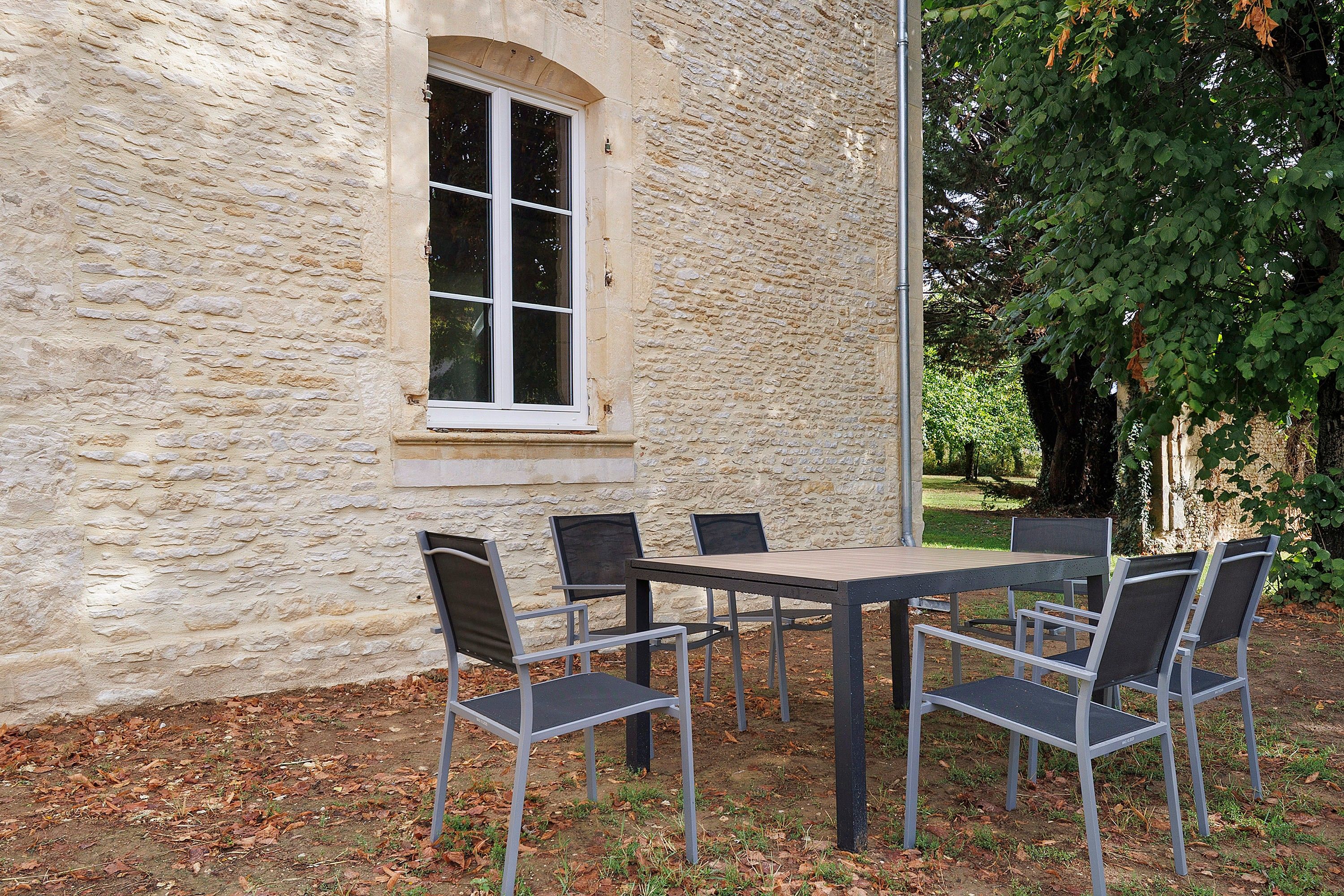 Een gebouw van steen met een raam en een tafel met stoelen er buiten.