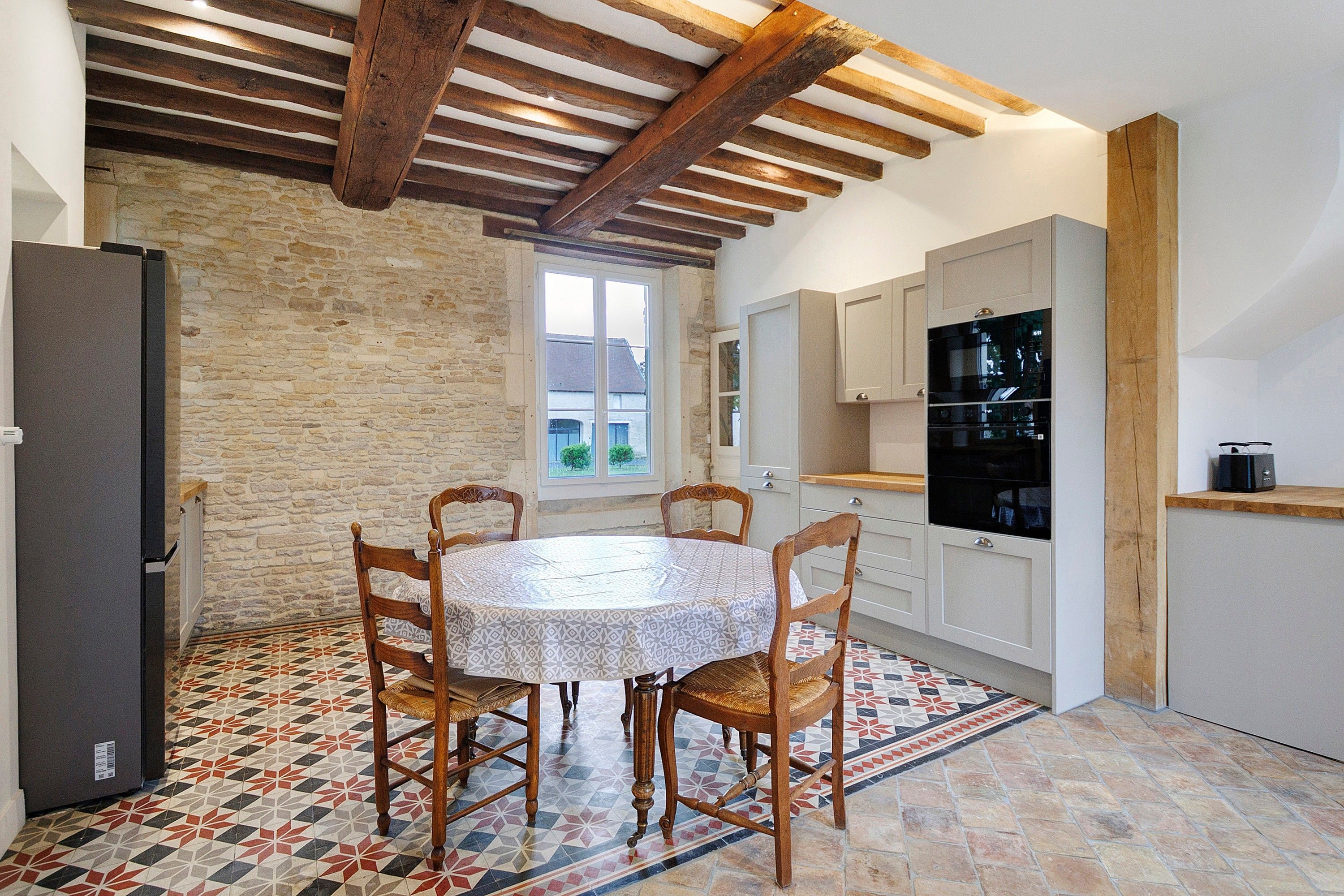 A kitchen with a round table, wooden chairs, a tiled floor, and a stone wall.