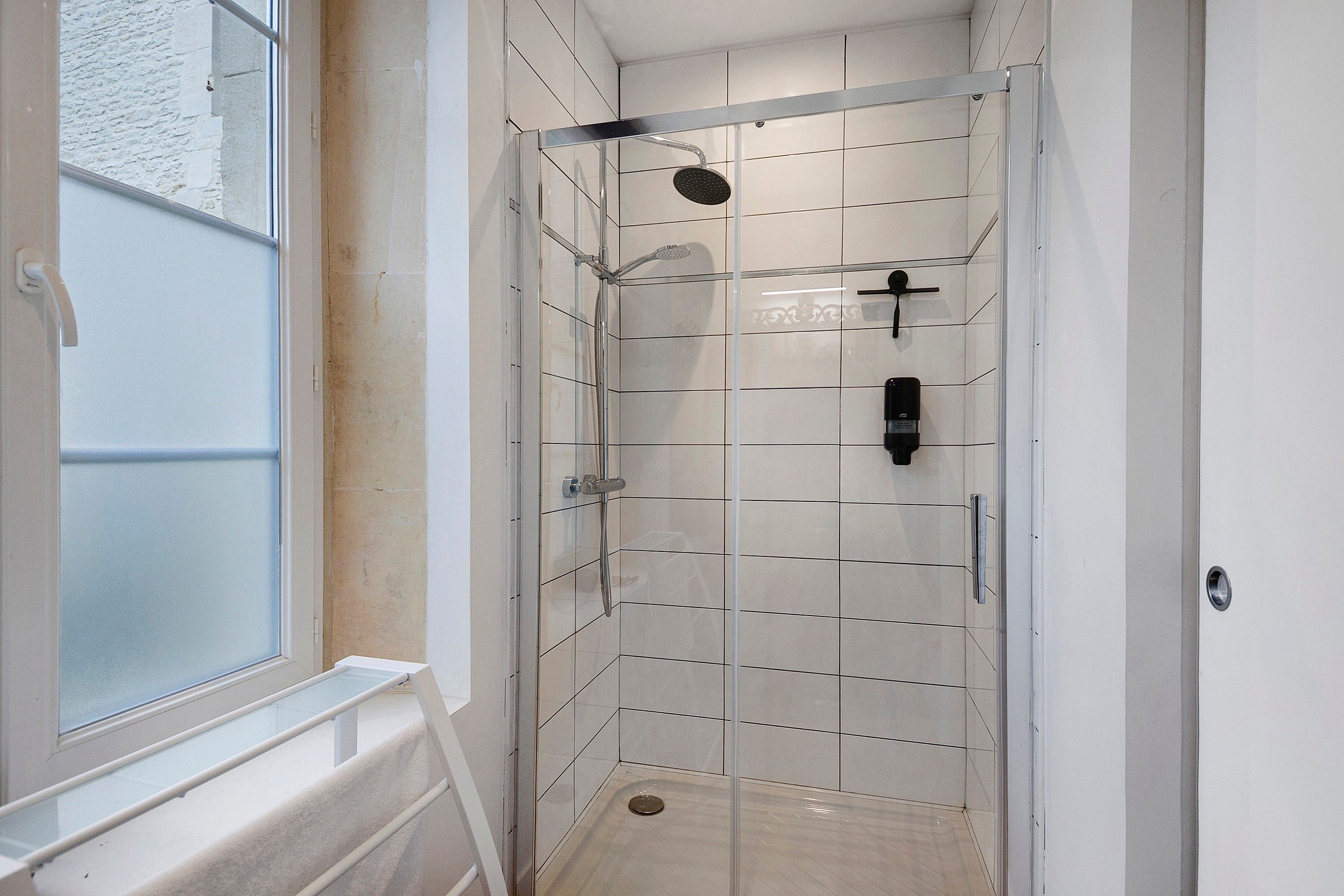 A shower with a glass door, a handheld showerhead, and a wall-mounted faucet.