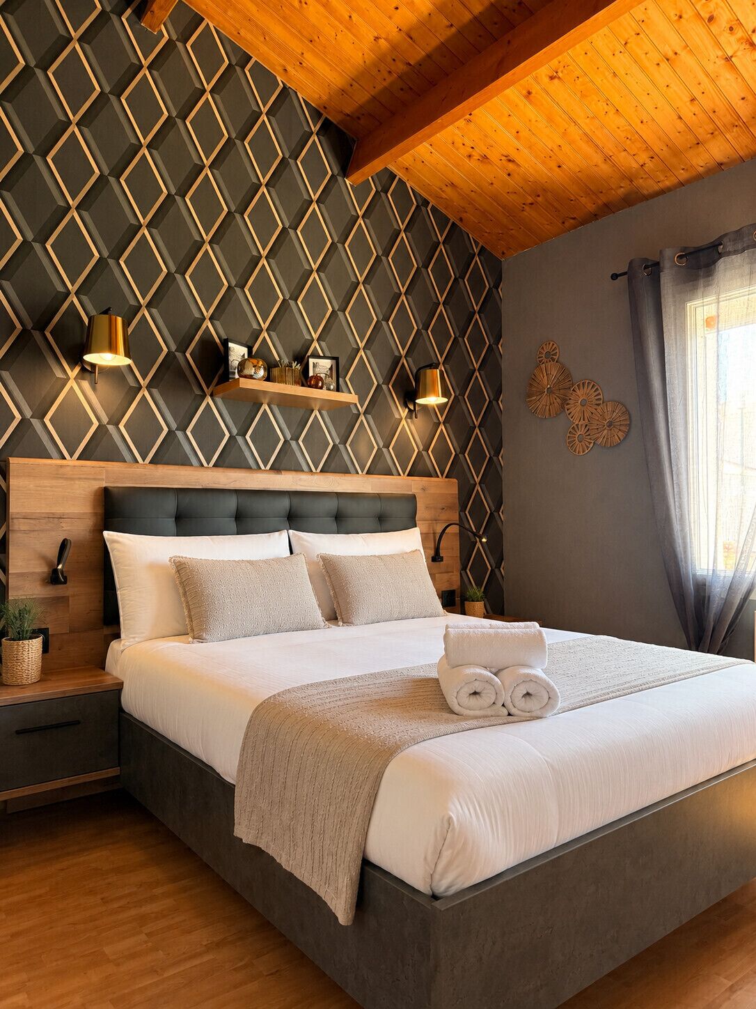 Ein modernes Schlafzimmer mit Wand im geometrischen Muster, einem Holzkopfteil, einem Bett mit weißer Bettwäsche, zwei Nachttischlampen und einem Fenster mit Vorhängen.
