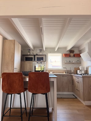 Eine moderne Küche mit Holzausstattung, einer zentralen Kochinsel, zwei Barhocker und einem Fenster mit Tageslicht.