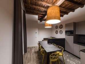 A compact kitchen with a dining area, wooden ceiling beams, and a modern light fixture. - Dolcevita Panisperna 1 – Norma Apartment (Rome)