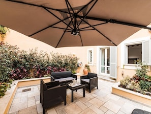 Eine Terrasse im Freien mit Tisch, Stühlen, einem großen Sonnenschirm und verschiedenen Pflanzen.