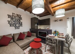 Ein modernes Wohnzimmer mit einer Couch, roten Akzenten, einem Esstisch mit Stühlen und einer Küche im Hintergrund.