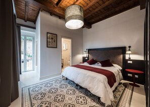 Ein Schlafzimmer mit einem großen Bett, einem gemusterten Teppich, einer Holzbalkendecke und einer Tür zu einem Badezimmer.