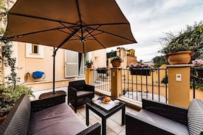 Ein Balkon mit Korbmöbeln, einem Tisch mit Früchten und Blumentöpfen.