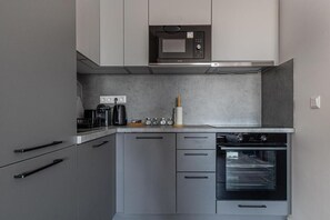 Une cuisine moderne avec des meubles de couleur grise, un four à micro-ondes encastré, une machine à café et une cuisinière.