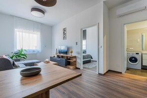 Un salon moderne avec un canapé, un téléviseur et une table à manger. Il y a également un espace buanderie avec un lave-linge et un sèche-linge.
