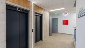 A modern elevator area with three elevators, a fire alarm, and a hallway with a tiled floor.