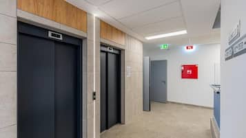 Ein moderner Aufzugsbereich mit drei Aufzügen, einem Brandmelder und einem Flur mit Fliesenboden.