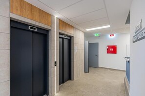 Ein moderner Aufzugsbereich mit drei Aufzügen, einem Brandmelder und einem Flur mit Fliesenboden.