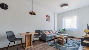 A modern living room with a sofa, two chairs, a coffee table, a dining table, a clock, a painting, and a window with curtains.