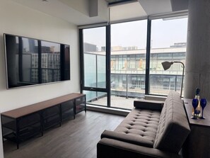 Ein modernes Wohnzimmer mit einem großen Flachbildfernseher, einer Couch, einer Bank und einem Tisch mit zwei Gläsern.