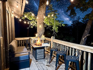 An outdoor deck with a fire pit, seating, and string lights against a night sky.