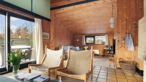 Un interior de madera con sofá, dos sillones, una mesa de comedor, una zona de bar y vistas a través de amplias ventanas.