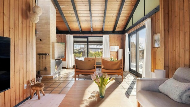 Un salón acogedor con paredes de madera, una chimenea, dos sofás y un ventanal con vistas al exterior.