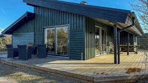 Una casa moderna de madera con terraza, puertas corredizas de vidrio y mobiliario exterior.