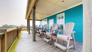 Ett trädäck med Adirondack-stolar, en inglasad veranda och utsikt över havet.
