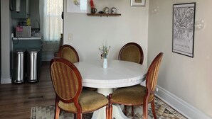Un coin repas avec une table ronde, quatre chaises, un ventilateur de plafond et une cuisine en arrière-plan.