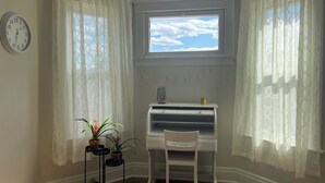 Une pièce d’angle comprenant un bureau, une chaise, des plantes en pot, une horloge et une fenêtre avec des rideaux.
