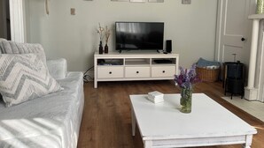 Un salon avec un canapé, une table basse, un téléviseur posé sur un meuble blanc et des œuvres d’art accrochées au mur.