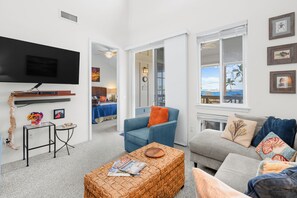 A living room with a flat-screen TV, a coffee table, and a sofa. - Alii Cove#EE22: Top Floor unit with Loft, Ac, Ocean Views, Sleeps 6! (Kailua Kona)