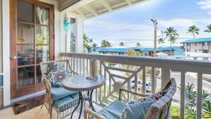 Un balcon agrémenté de meubles en osier, une petite table ronde et une vue sur une zone côtière avec des bâtiments et des palmiers.