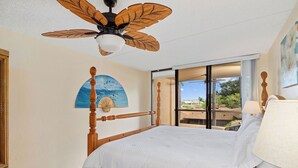 Un dormitorio con cama de madera, ventilador de techo, un cuadro, ventana con vistas y una lámpara.